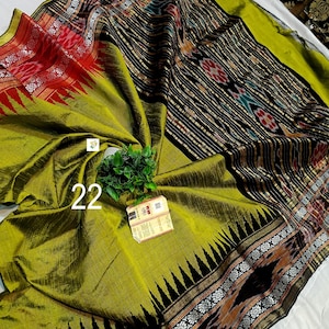 May include: A lime green saree featuring a black border with white floral patterns and red accents. The fabric displays a textured weave with a central panel of black and white vertical stripes, interspersed with geometric motifs and the number 22.