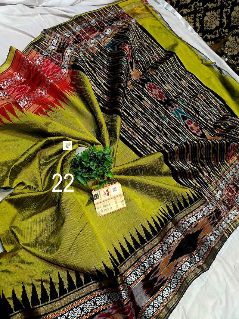 May include: A lime green saree featuring a black border with white floral patterns and red accents. The fabric displays a textured weave with a central panel of black and white vertical stripes, interspersed with geometric motifs and the number 22.