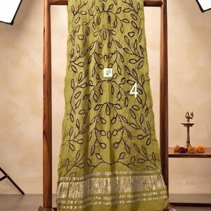 May include: An olive green scarf featuring a dark brown embroidered vine and leaf pattern throughout. The bottom edge is finished with a wide, metallic silver border. The number 4 is printed in white on the center of the fabric.
