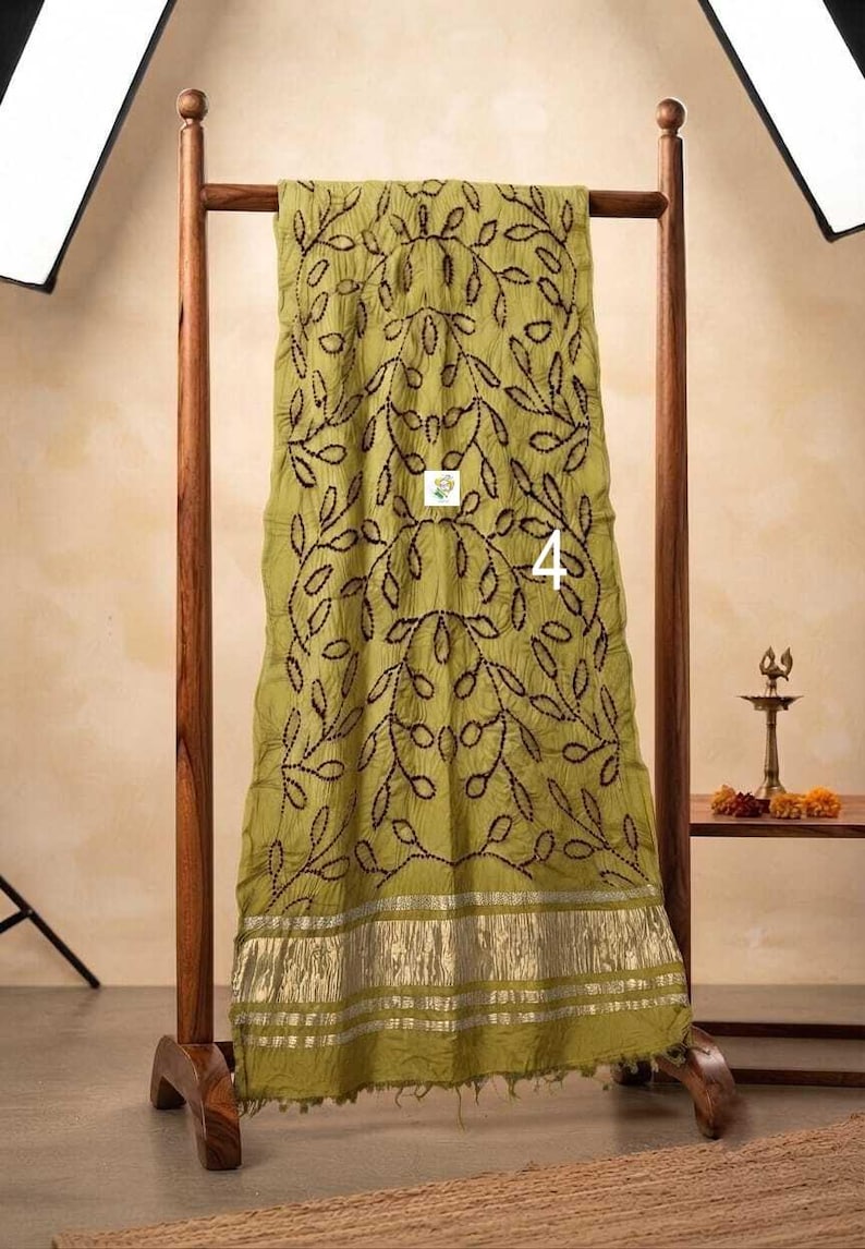 May include: An olive green scarf featuring a dark brown embroidered vine and leaf pattern throughout. The bottom edge is finished with a wide, metallic silver border. The number 4 is printed in white on the center of the fabric.