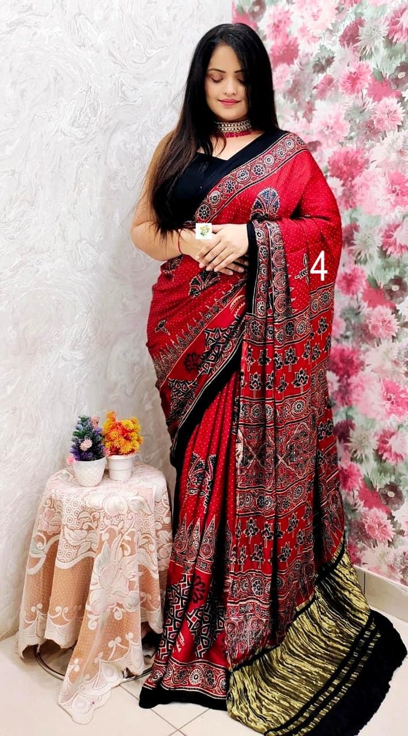 May include: A red saree featuring a black and white block-print pattern with floral motifs, a solid black border, and a metallic gold pleated hem. The garment is paired with a sleeveless black blouse and includes the number 4 printed on the fabric.