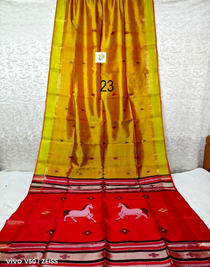 Puede incluir: Un sari de colores amarillo y rojo vibrantes que presenta una secci&oacute;n superior de color amarillo dorado con peque&ntilde;os motivos de diamantes oscuros y una secci&oacute;n inferior de color rojo brillante con dos figuras de caballos blancos y bordes.