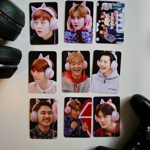Puede incluir: Nueve tarjetas fotográficas rectangulares con diferentes personas que usan auriculares rosas con orejas de gato. Las personas son de ascendencia asiática y están sonriendo. Las tarjetas están sobre una superficie blanca con un mando de juegos y auriculares negros.