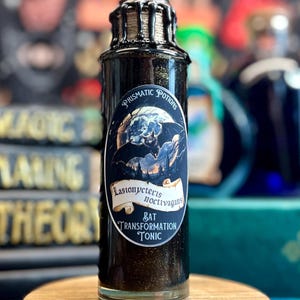 May include: A dark glass bottle with a black wax seal and a label that reads "Prismatic Potions." The label features an illustration of a bat and the text "Lasionycteris Noctivagans Bat Transformation Tonic." The bottle sits on a small, round wooden stand.