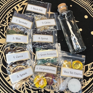May include: A set of ten small clear plastic bags containing various herbs, crystals, and dried flowers. Each bag is labeled with a number and the name of the item inside. The items include black salt, lavender, mint, cloves, lemon, green aventurine, garnet, chrysanthemum, and citrine. There is also a clear glass bottle with a cork stopper and a small bag containing a white candle, a gold metal dish, and a white spoon. The bag is labeled "Wax Kit/Charms".