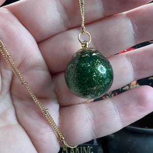 Puede incluir: Un collar de cadena dorada con un colgante de orbe lleno de purpurina verde.