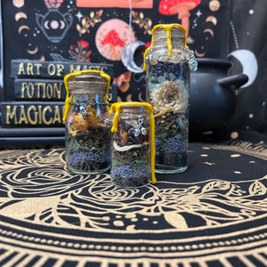May include: Three glass bottles filled with dried flowers, herbs, and spices. The bottles are sealed with yellow wax and have a rustic, witchy aesthetic.