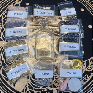 May include: A collection of ingredients and tools for spell casting, including pink salt, lavender, rosemary, calendula, dried lemon, a key, amethyst, obsidian, a bottle of liquid, charms, and a wax kit.