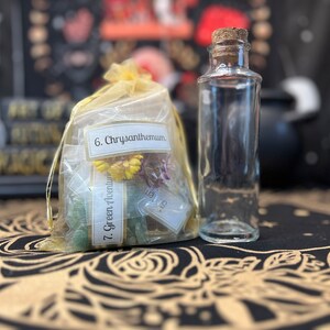 May include: A clear glass bottle with a cork stopper, next to a yellow organza bag filled with dried flowers and green crystals. The bag has labels that read "6. Chrysanthemum" and "7. Green Aventurine".
