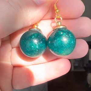 May include: A pair of gold hoop earrings with green glitter balls. The balls are about 1 inch in diameter.