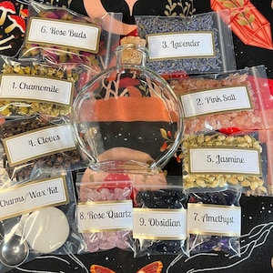 May include: A collection of dried herbs, crystals, and a glass bottle with a cork stopper. The herbs are labeled with numbers and names: 1. Chamomile, 2. Pink Salt, 3. Lavender, 4. Cloves, 5. Jasmine, 6. Rose Buds. The crystals are labeled: 7. Amethyst, 8. Rose Quartz, 9. Obsidian. The bag labeled "Charms/Wax Kit" contains a small white disc and a spoon.
