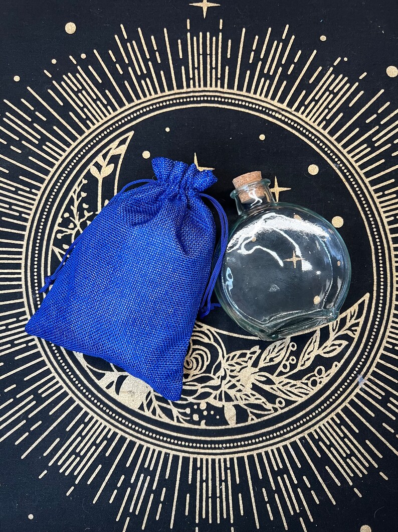 May include: A blue burlap pouch and a clear glass bottle with a cork stopper, both sitting on a black background with a gold sunburst design.