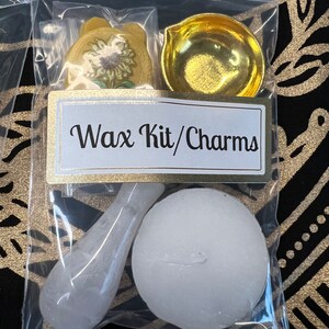 May include: A clear plastic bag containing a wax kit and charms. The kit includes a small white round wax block, a white spoon-shaped tool, a gold-colored metal dish, and a yellow paper charm with a sunflower design. The bag has a label that reads "Wax Kit/Charms".