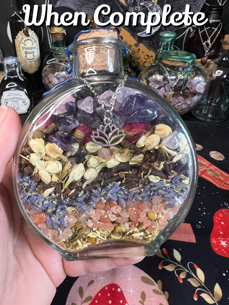 May include: A clear glass bottle filled with dried herbs, flowers, and crystals. The bottle has a cork stopper and a silver chain with a lotus charm hanging from it. The bottle is sitting on a black and red patterned surface.