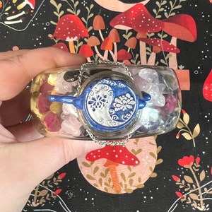 May include: A clear glass jar filled with colorful crystals and a blue and white yin yang charm. The jar is decorated with a silver chain.