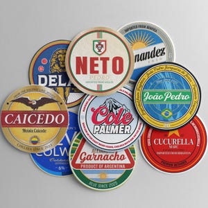 Op de afbeelding: Een verzameling ronde onderzetters met diverse ontwerpen en tekst. De onderzetters tonen namen als "NETO", "CAICEDO" en "Cole Palmer". Sommige onderzetters bevatten teamlogo's en nationale vlaggen. De onderzetters zijn waarschijnlijk voor drankjes.