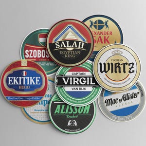 Może przedstawiać: Kolekcja okrągłych podkładek pod szklanki z różnymi wzorami i tekstami. Podkładki zawierają nazwiska takie jak "SALAH", "VIRGIL" i "WIRTZ", a także frazy takie jak "Egyptian King" i "Red Since 2023". Podkładki są w różnych kolorach.