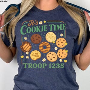 Puede incluir: Camiseta azul marino con el texto "It's Cookie Time" e ilustraciones de diferentes galletas. La camiseta tambi&eacute;n muestra "TROOP 1235". El dise&ntilde;o incluye elementos florales y corazones.