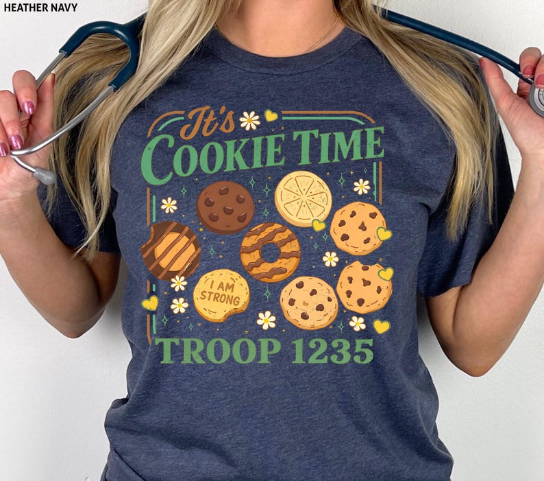 Puede incluir: Camiseta azul marino con el texto "It's Cookie Time" e ilustraciones de diferentes galletas. La camiseta tambi&eacute;n muestra "TROOP 1235". El dise&ntilde;o incluye elementos florales y corazones.