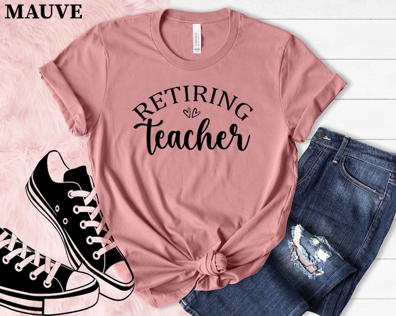 以下が含まれることがあります： 「Retiring Teacher」の黒い文字がプリントされた、モーヴ色のTシャツ。青いジーンズと白と黒のスニーカーが写っています。Tシャツはウエストで結ばれています。