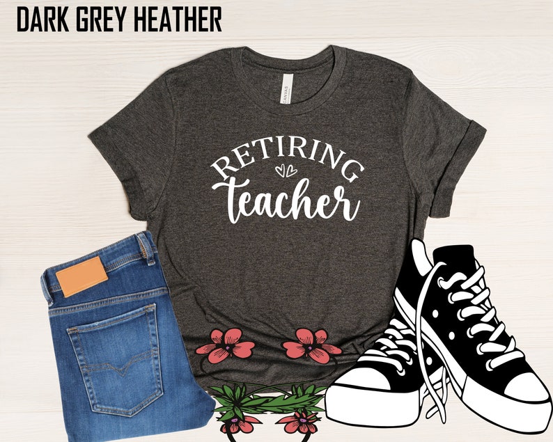 以下が含まれることがあります： 「Retiring Teacher」の文字が白で書かれたダークグレーヘザーTシャツ。画像には、青いジーンズと白と黒のスニーカーも含まれています。