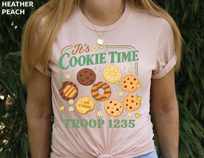 Puede incluir: Camiseta melocot&oacute;n claro con el texto "It's Cookie Time" en verde y naranja. La camiseta presenta ilustraciones de varias galletas y el texto "TROOP 1235".