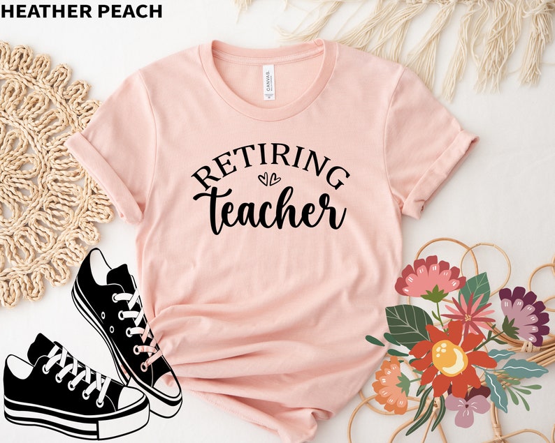 以下が含まれることがあります： 「Retiring Teacher」の黒い文字が書かれた、ヘザーピーチ色のTシャツ。 黒と白のスニーカーと花の配置でスタイリングされています。 画像の左上隅には「HEATHER PEACH」という文字があります。
