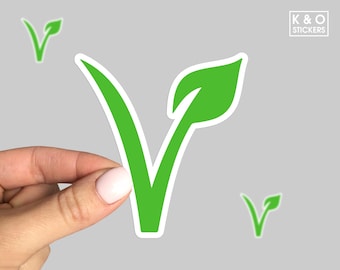 May include: A green vegan sticker in the shape of a leaf with a white border, held by a hand. The sticker has a large "V" shape with a leaf at the top. Two smaller matching stickers are also visible. The text "K & O STICKERS" is in the upper right corner.