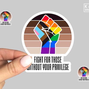 May include: A round sticker featuring a raised fist in rainbow colors, with a brown and tan striped background. The text "FIGHT FOR THOSE WITHOUT YOUR PRIVILEGE" is below the fist. The sticker is held by a hand.
