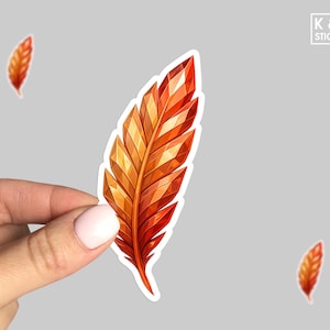 May include: A vibrant sticker featuring a stylized feather in shades of orange and red, held by a hand. The feather design has a geometric, faceted appearance. The sticker has a white border and the text "K & O STICKERS" is in the upper right corner.