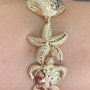 May include: Gold bracelet with a seashell, starfish, and turtle design. The bracelet is made of 14k gold and has a polished finish.
