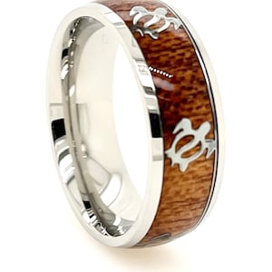 May include: A silver ring with a wide band featuring a wood inlay. The wood is a rich brown colour and is accented with silver sea turtle cutouts. The ring has a polished, reflective finish.
