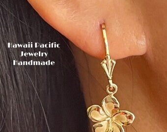 May include: Gold flower dangle earrings with a simple hoop design. The earrings feature a delicate plumeria flower charm.