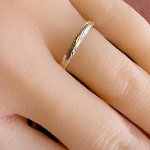May include: A thin silver band with a gold-toned design. The band is worn on a finger.