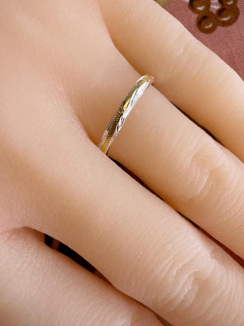 May include: A thin silver band with a gold-toned design. The band is worn on a finger.