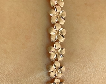 May include: A gold bracelet with a chain of small flower-shaped links. The bracelet is worn on a person's wrist.