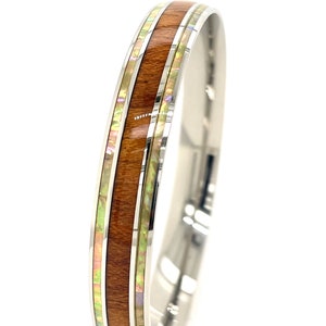May include: A stainless steel ring with a band of brown wood and iridescent green and white inlay.
