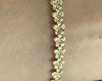 May include: A gold bracelet with a floral design. The bracelet is made of small, interconnected flower shapes.