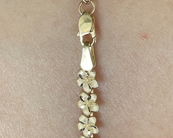 Puede incluir: Un collar de cadena de oro con un diseño de flores. La cadena está hecha de pequeñas flores delicadas que están unidas entre sí.