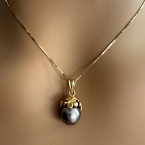 Puede incluir: Un collar de oro con un colgante con una perla gris oscuro. La perla est&aacute; encerrada en un dise&ntilde;o floral dorado, y la cadena es una delicada cadena de oro. El collar se muestra sobre un fondo neutro.
