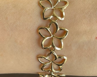 May include: A gold bracelet with a chain of linked flower-shaped charms. Each charm is a delicate, openwork design.