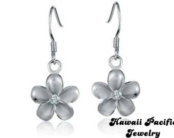 Può includere: Orecchini d'argento con un designo a forma di fiore bianco e un piccolo ciottolo trasparente al centro. Gli orecchini hanno la forma di un fiore di frangipane. Hawaii Pacific Jewelry.