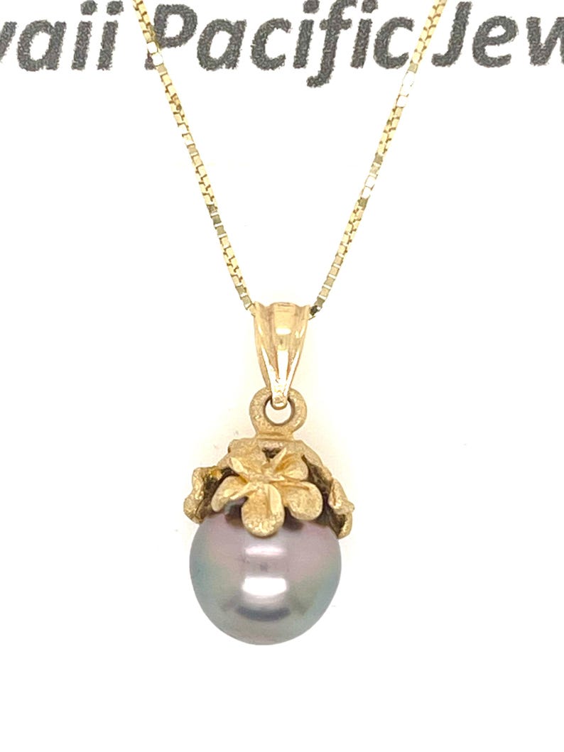 Puede incluir: Collar dorado con un colgante de perla gris. El colgante presenta un engaste en forma de flor. La cadena es una fina cadena de caja. El texto "Hawaii Pacific Jew" es visible en la parte superior.