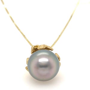 Puede incluir: Un collar de oro con un gran colgante de perla iridiscente. La perla tiene un suave tono gris-azul con un toque de rosa. El colgante est&aacute; unido a una delicada cadena de oro. El collar se muestra sobre un fondo blanco.