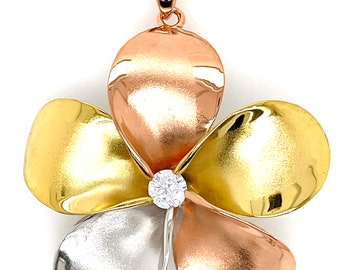 Puede incluir: Un collar con un colgante en forma de flor de plumeria de oro, plata y oro rosa, con una piedra de circonita cúbica transparente en el centro.
