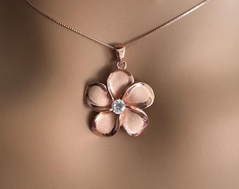 Puede incluir: Un collar de oro rosa con una cadena delicada y un colgante en forma de flor con un cristal transparente en el centro.