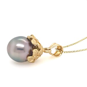 Puede incluir: Un collar con colgante de oro con una perla gris. La perla est&aacute; sujeta por un engaste dorado decorativo. La cadena del collar es de color dorado delicado, creando una elegante pieza de joyer&iacute;a.