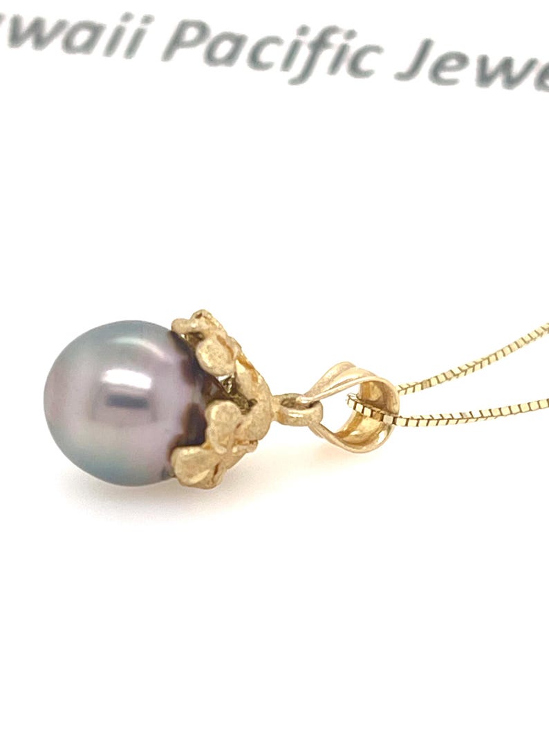 Puede incluir: Un collar con colgante de oro con una perla gris. La perla est&aacute; sujeta por un engaste dorado decorativo. La cadena del collar es de color dorado delicado, creando una elegante pieza de joyer&iacute;a.