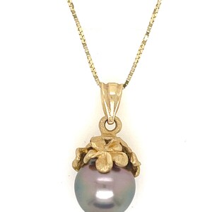 Puede incluir: Un collar dorado con un colgante con una perla gris oscura. La perla est&aacute; encerrada en un dise&ntilde;o floral dorado. La cadena es una delicada cadena dorada.