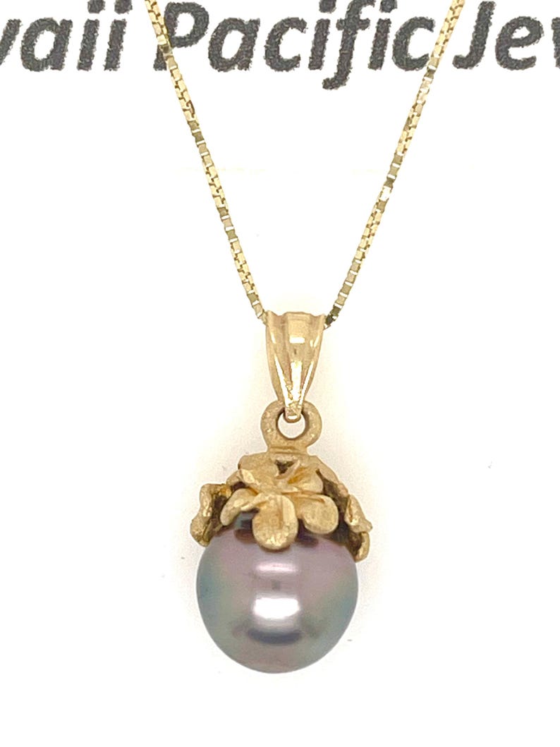 Puede incluir: Un collar dorado con un colgante con una perla gris oscura. La perla est&aacute; encerrada en un dise&ntilde;o floral dorado. La cadena es una delicada cadena dorada.